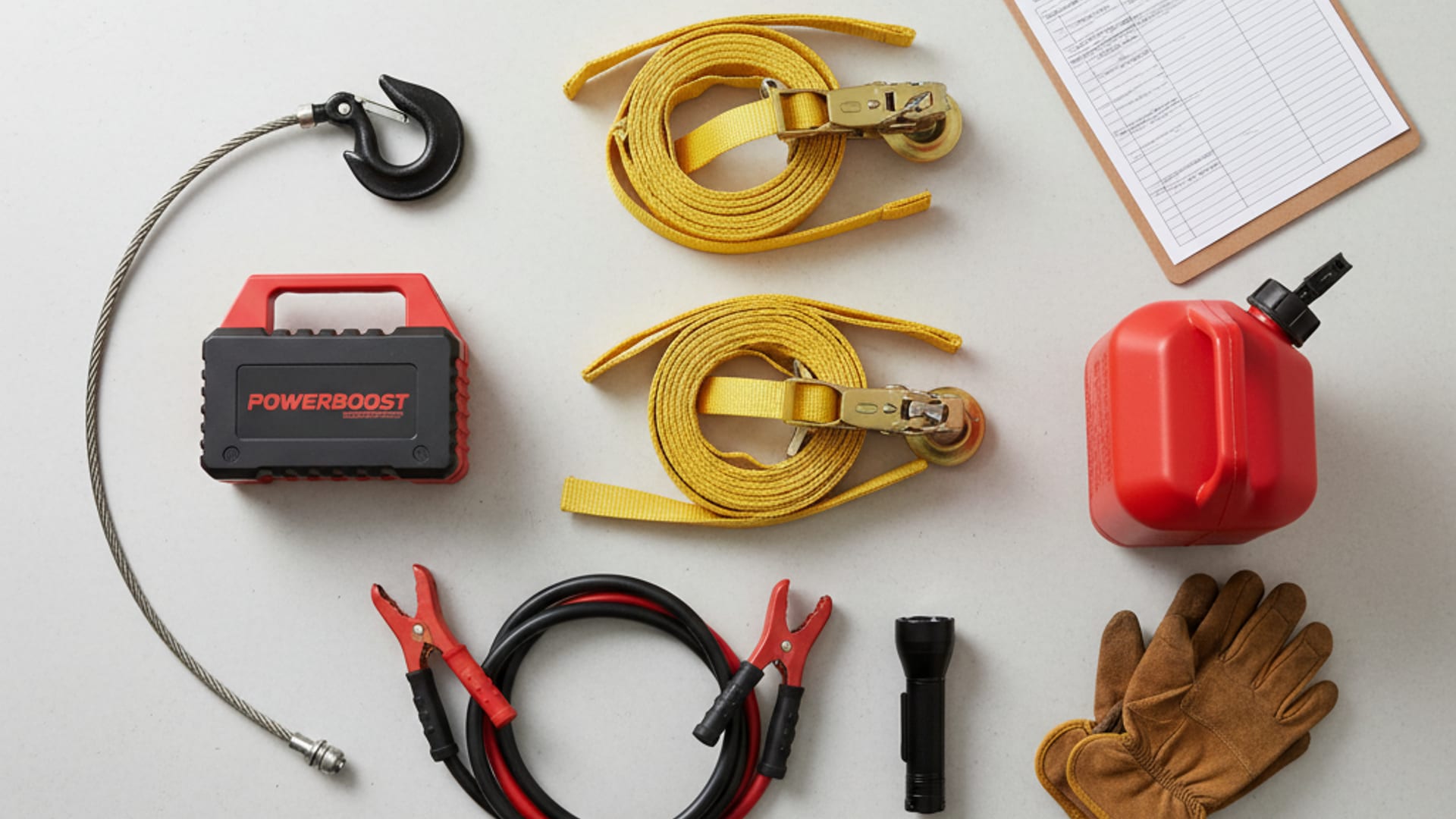 Overhead flat-lay of professional tow equipment including soft-strap wheel nets, jump pack, winch hook, jumper cables, and clipboard with service forms